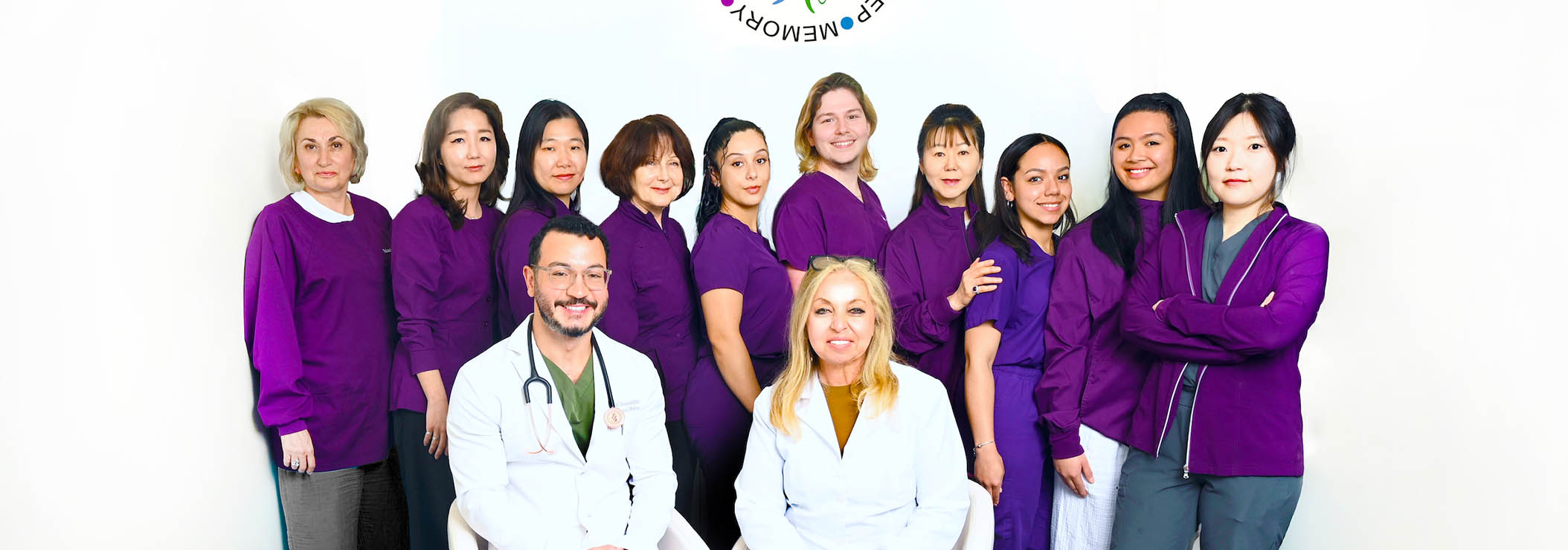 The image shows a group of people posing together, likely professionals given their attire, which includes scrubs and lab coats, suggesting they may be healthcare workers.